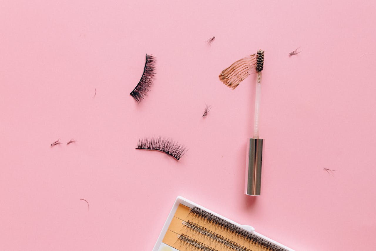 Styled flat lay of false eyelashes and makeup brush on a pastel pink surface.